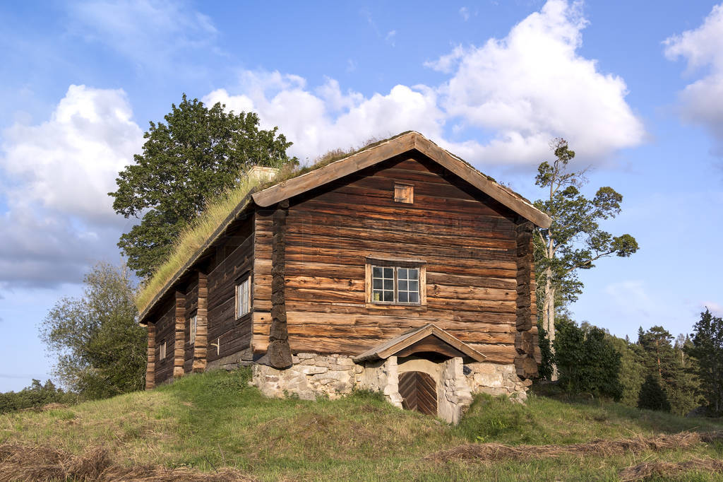 View of a very old log cabin. It stands on a small hill, in the