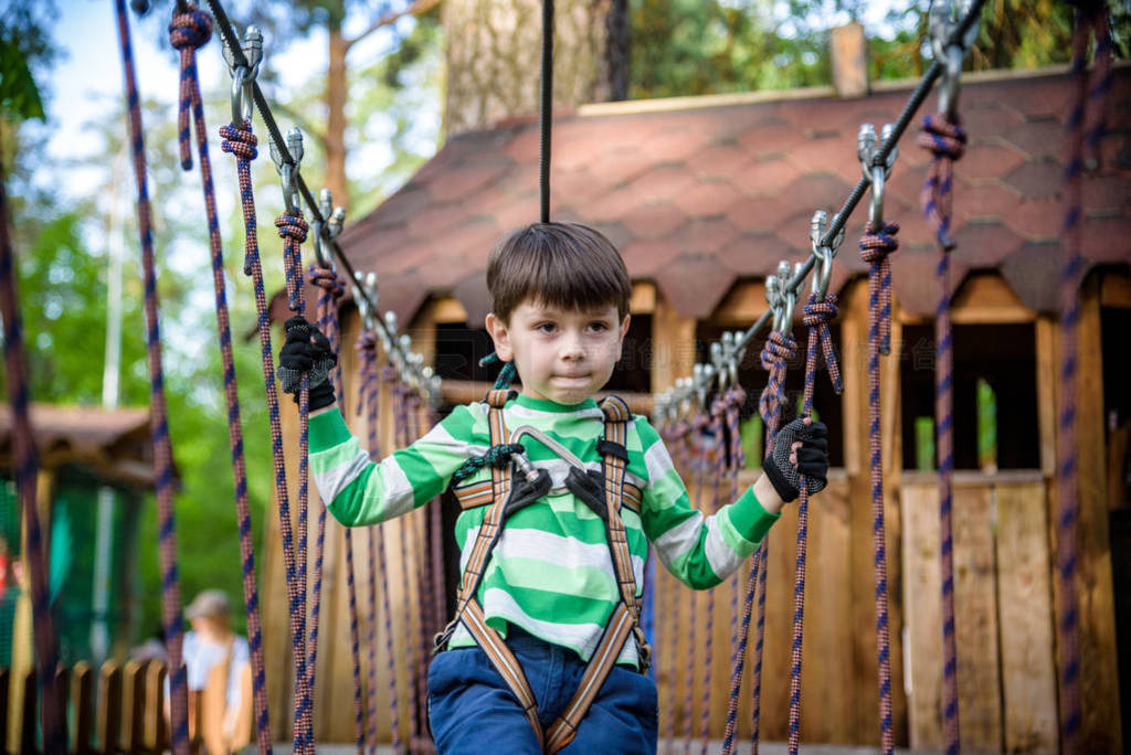 Happy kid playing at adventure park, holding ropes and climbing
