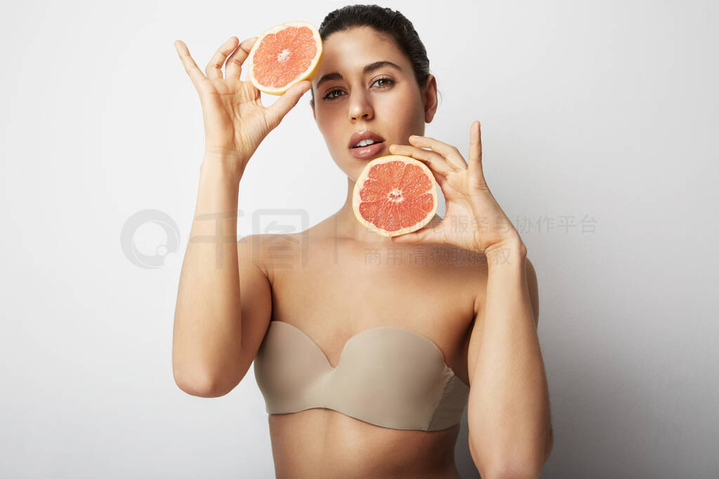 Portrait of young beautiful woman with two oranges posing over w