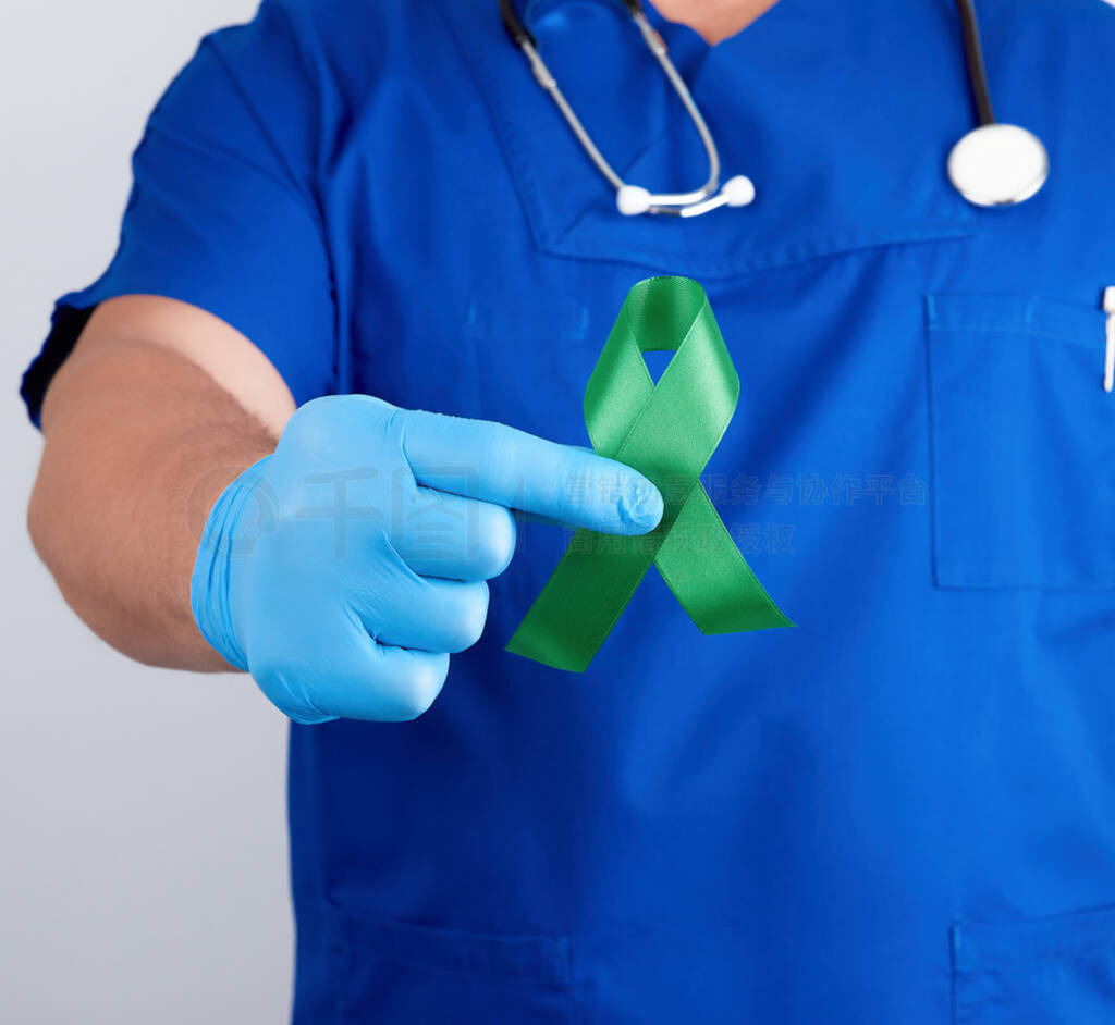 doctor in blue uniform and latex gloves holds a green ribbon