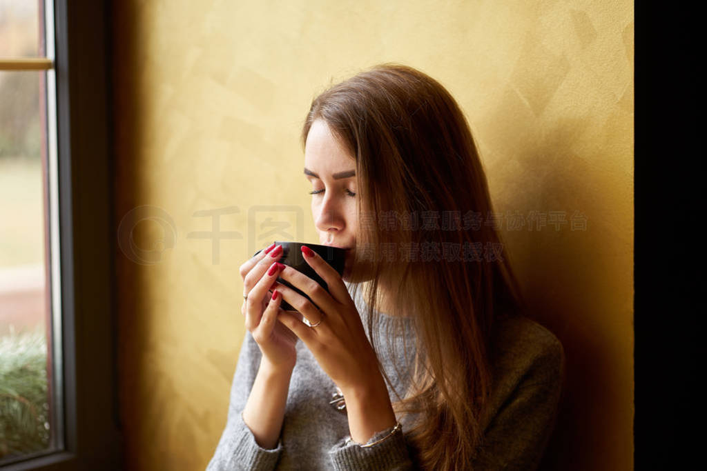 Young pretty girl with long hair drinking coffee or tea in the