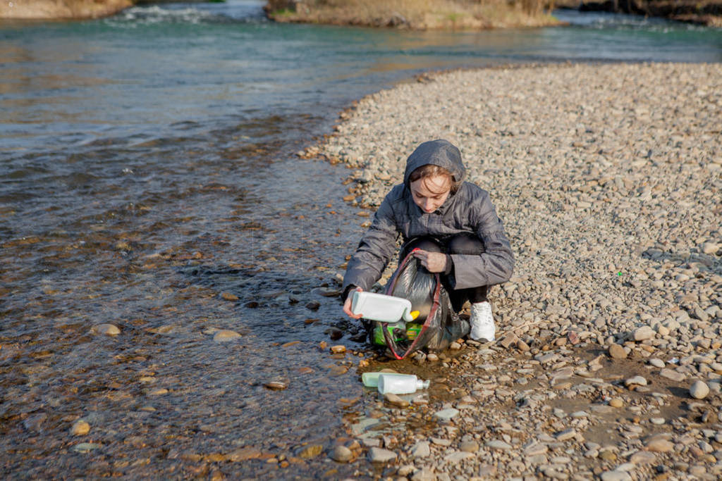 Young woman collecting plastic trash from the beach and putting