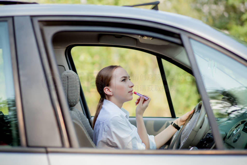 Picture of young businesswoman doing makeup while driving a car