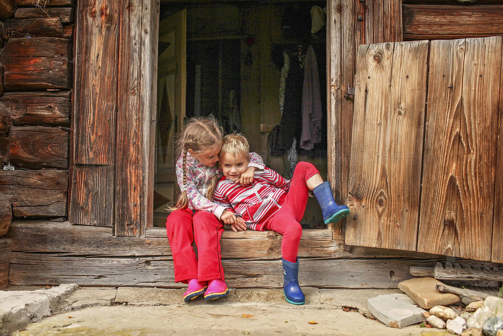 Children having rest on the doorstep of old wooden house during