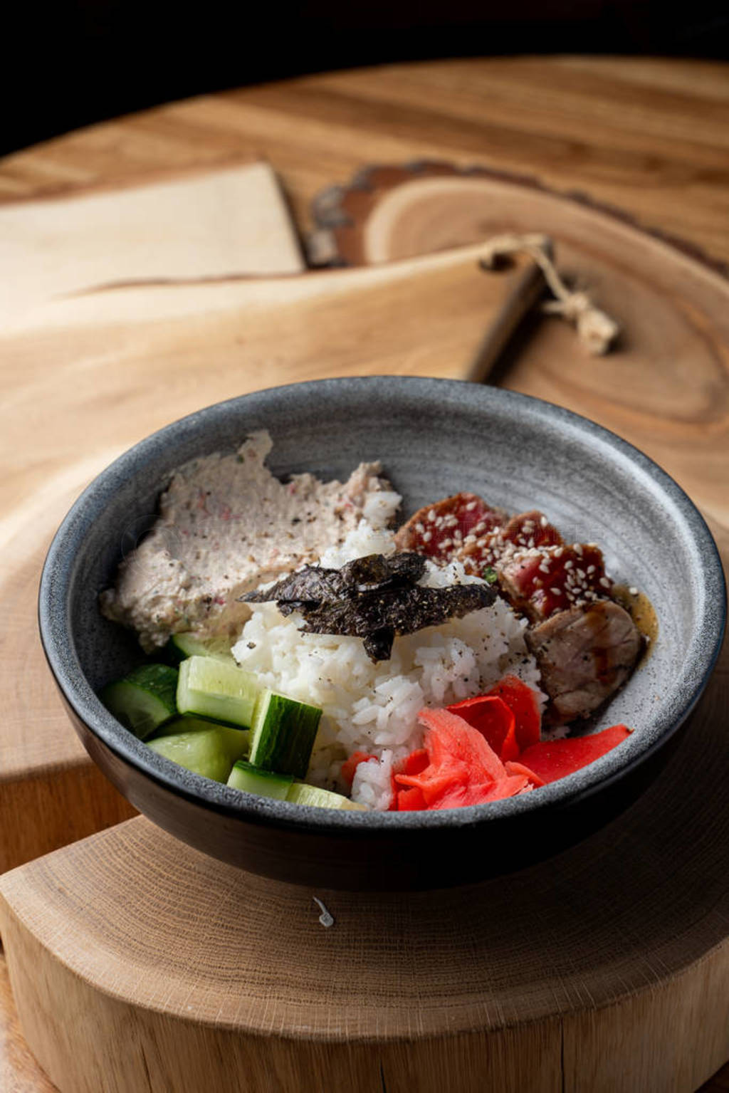 Tuna poke bowl with white rice, ginger and cucumber on wooden ru