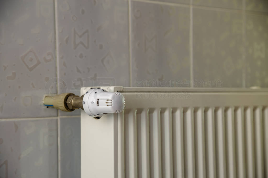 Heating radiator with thermostat valve on light wall tiles copy