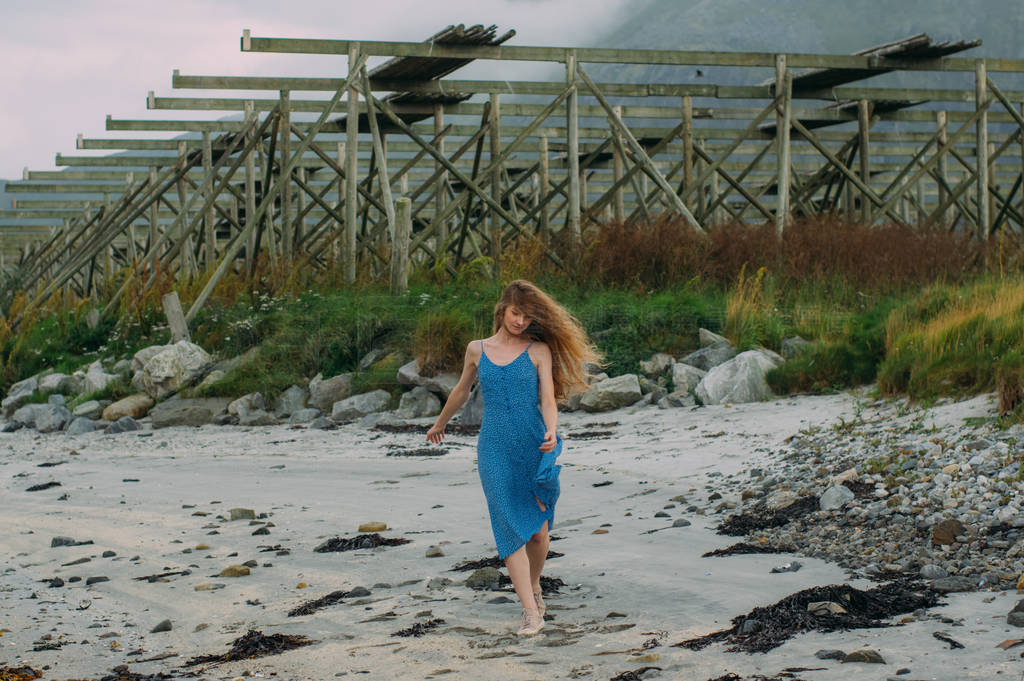 Young woman in blue dress walking on white sand, fish dryers