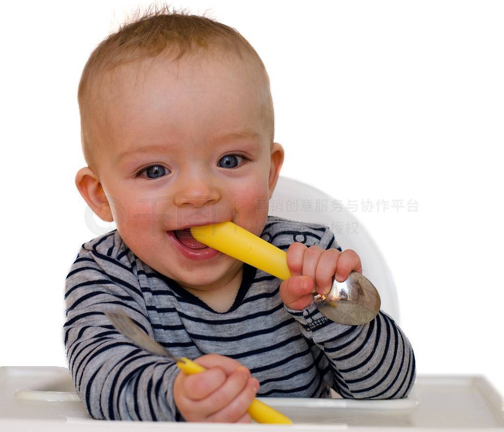 Happy baby boy is prepared to eat lunch with fork and spoon.