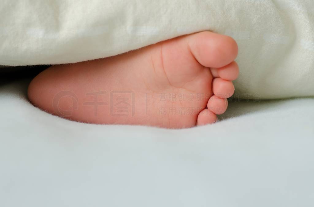 Cute feet of sleeping toddler poking of a white blanket.