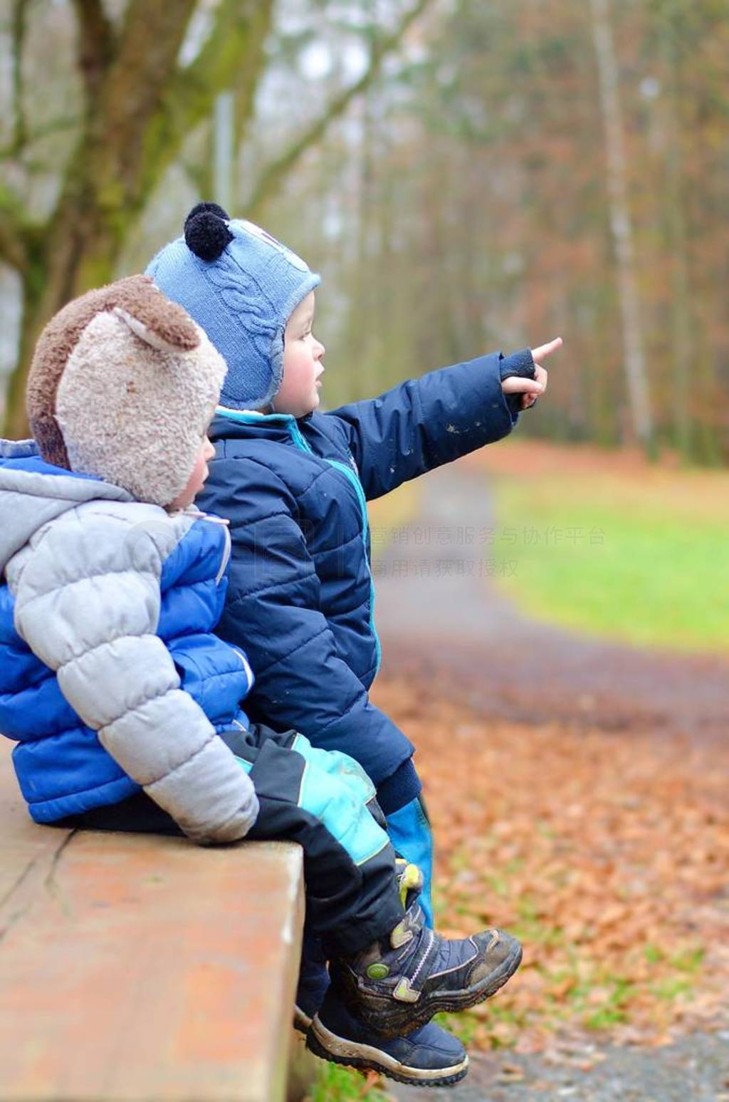 Brothers are sitting on a bench. Older one shows younger brother