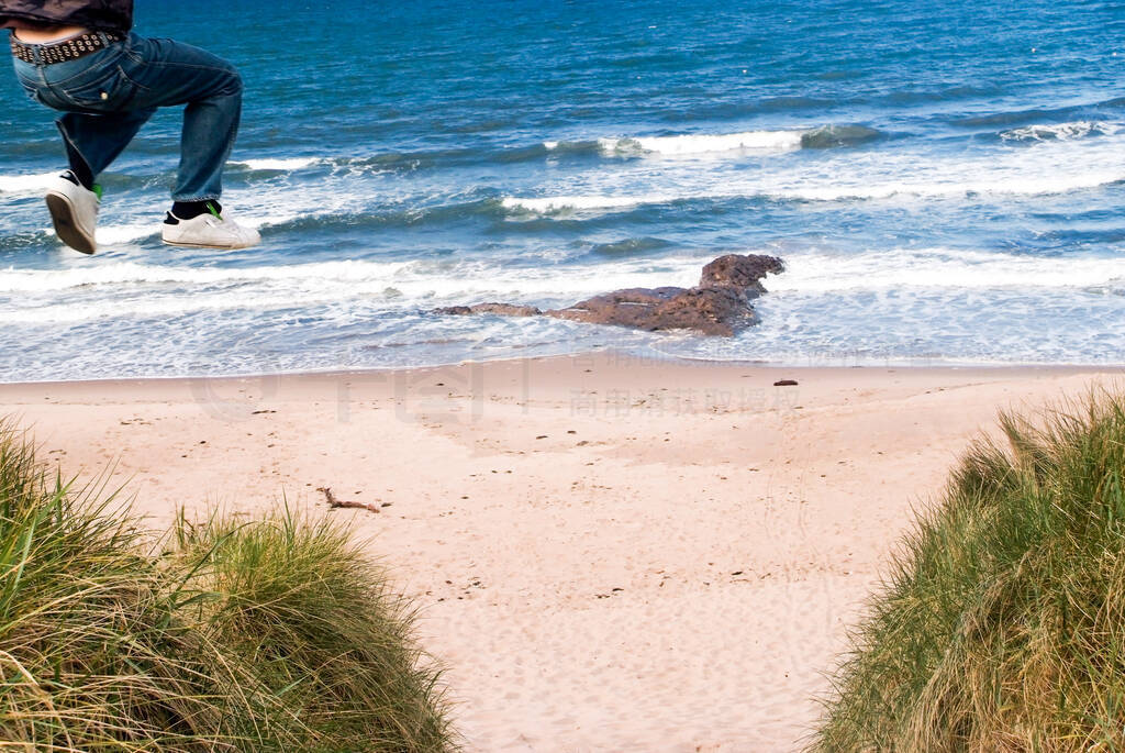 Man jumping from a high sand dune to the sand on the beach on a