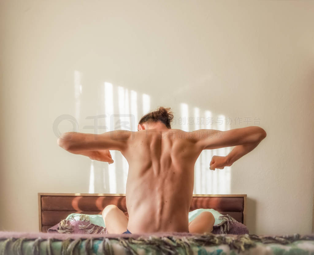 Back view of a Caucasian, naked man waking up in bed and stretch