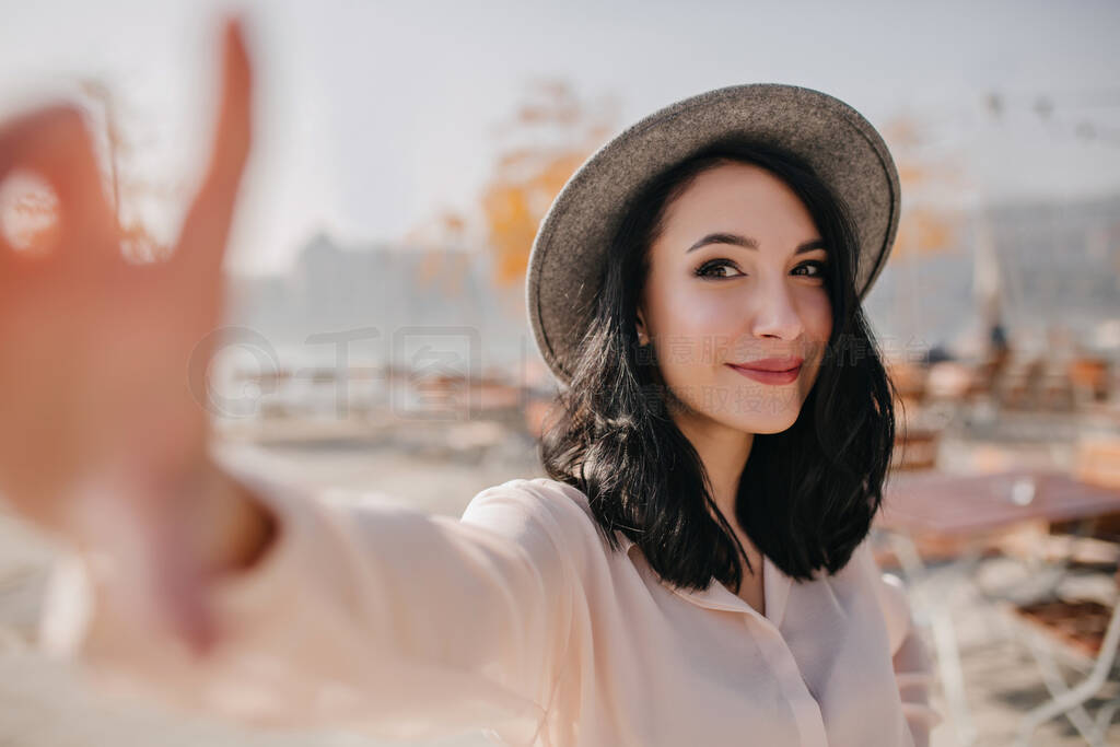 Emotional brunette girl in stylish hat making selfie in warm day