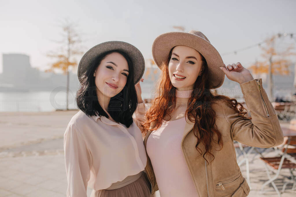 Elegant red-haired woman in beige outfit posing with friend on n