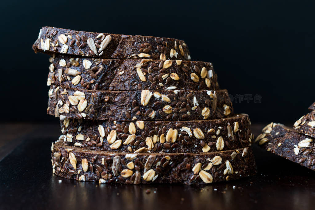 Malt Bread Slices with Oat and Flax Seeds on Dark Wooden Board.