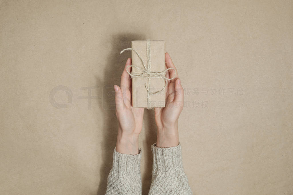 Human hands gives away a gift in brown paper on matching backgro