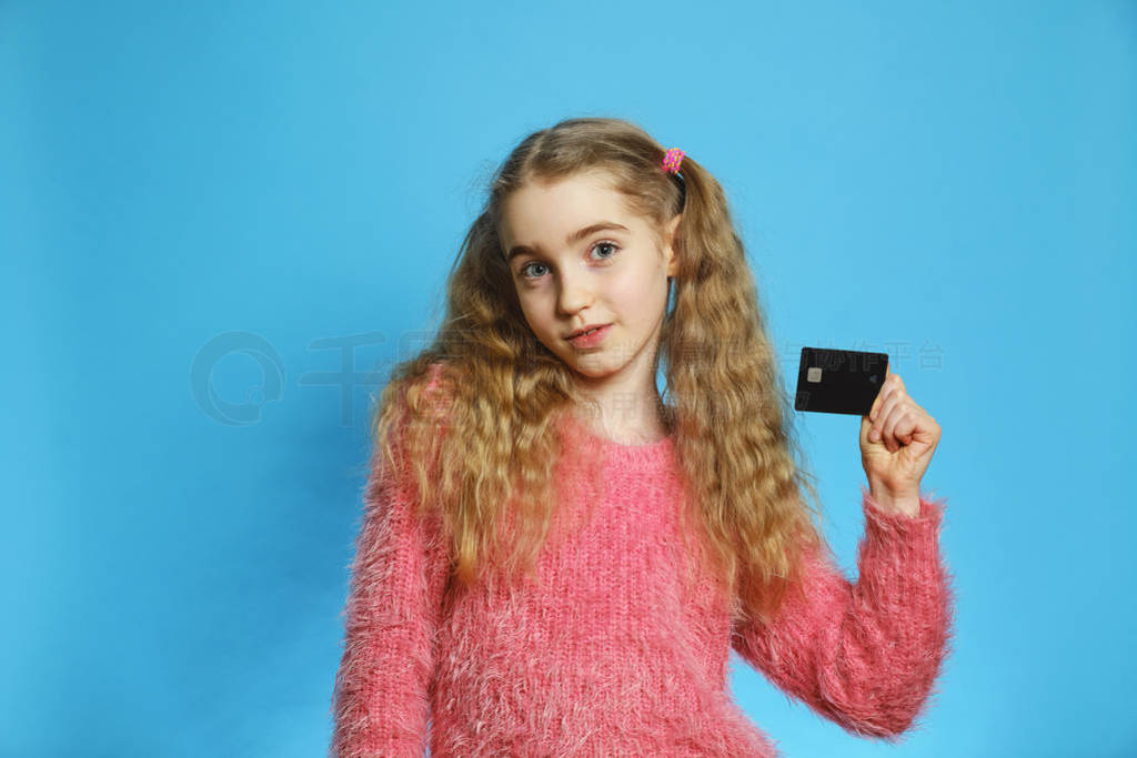 Little girl with a bank card. Joyful girl isolated on a blue bac