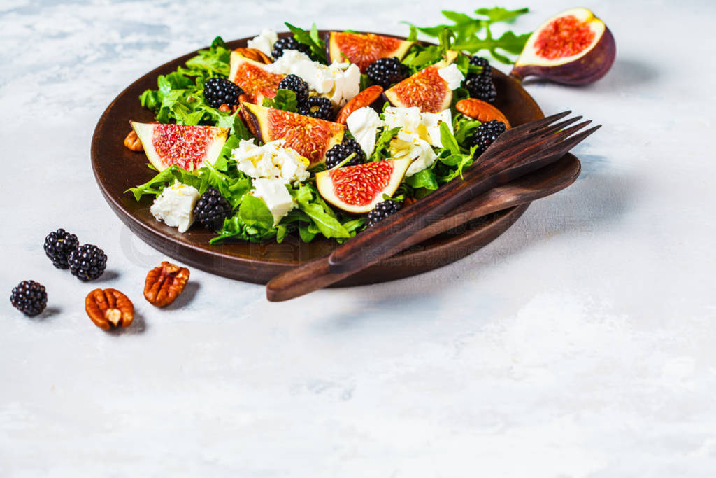 Salad with figs, feta cheese and blackberries in a wooden plate