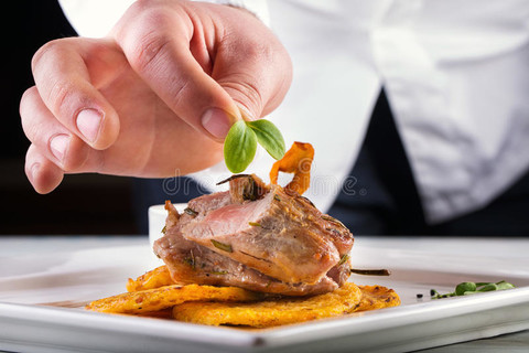 厨师在酒店或餐厅厨房烹饪，只有手。 用土豆或芹菜煎饼准备肉牛排。