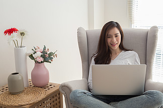 年轻的亚洲女性穿着休闲服 在公寓里工作时使用笔记本电脑检查电<i>子</i><i>邮</i>件和微笑在家工作或自我隔离 隔离和待在家里的概念