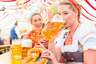 在慕尼黑啤酒节的帐篷里喝巴伐利亚啤酒的妇女或穿着紧身裙的成<i>年</i>人
