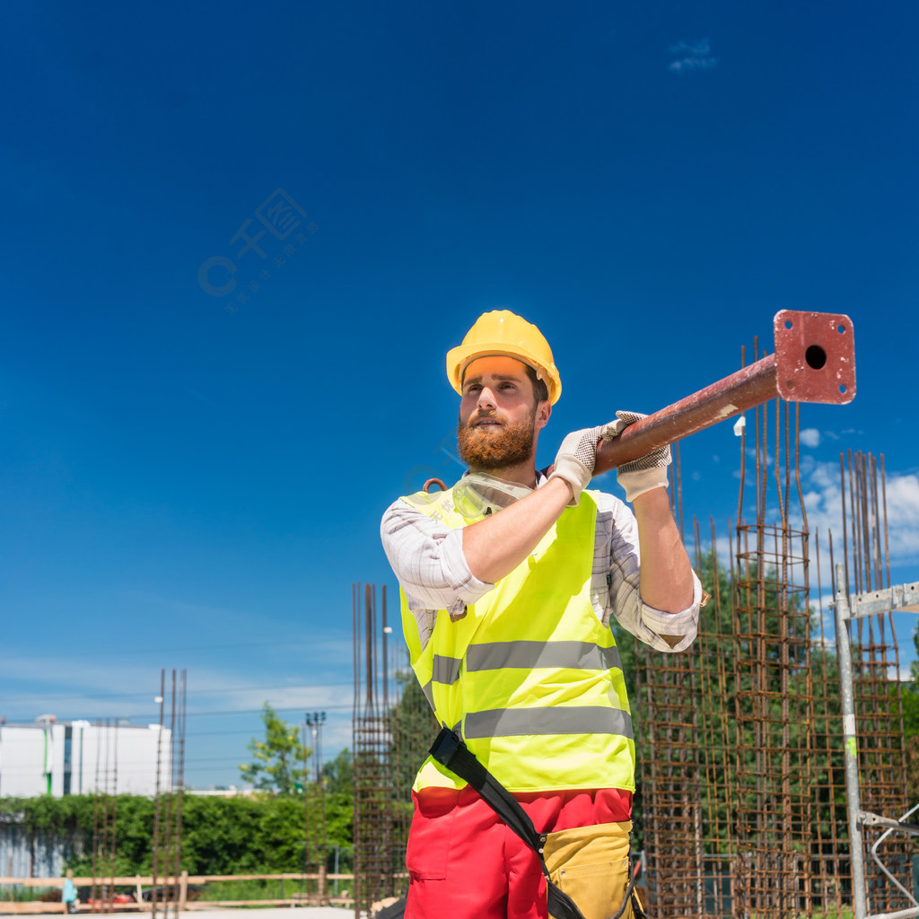 一名蓝领工人穿着安全设备在住宅建筑工地工作时携带重型金属棒的全长