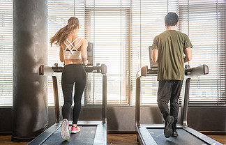 在健身房锻炼<i>期</i>间在跑步机上跑步的年轻男女的全长后视图