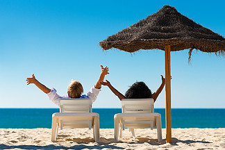 一对夫妇坐在沙滩上遮阳伞下的太阳椅上伸展双臂 感觉自由