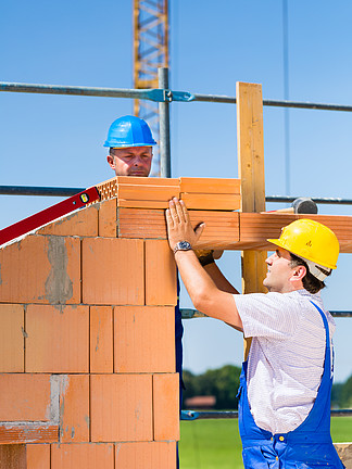 兩名瓦工或建築工或工人在建築或建築工地建造或砌磚或鋪設石牆或磚牆