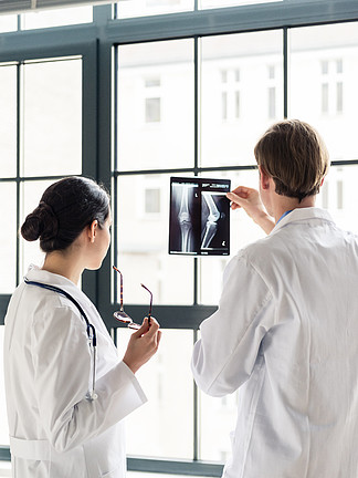 经验丰富的男性骨科医生帮助他的女同事解<i>释</i>办公室患者膝盖的 X 光片