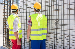 两名蓝领工人穿着安全设备 同时检查钢结构的耐久性 用于加固在建建筑物的墙壁