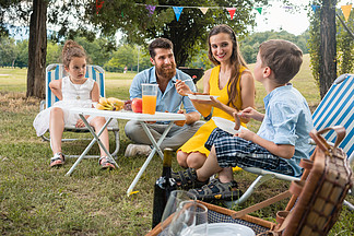 在夏日的家庭野餐期间 两个孩子的<i>敬</i><i>业</i>的年轻父母在听他们有趣的儿子说话时一起吃饭