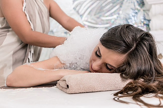 在传统土耳其浴中刺<i>激</i>泡沫按摩时 年轻女子在热大理石桌上放松