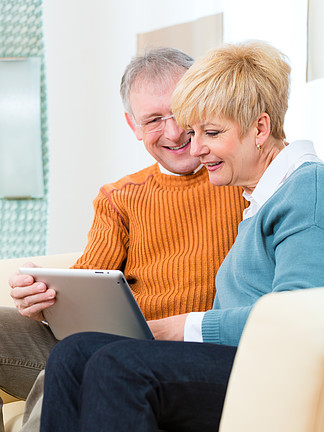 生活质量 — 两个老人坐在家里的沙发上 在平板电脑上写电<i>子</i><i>邮</i>件