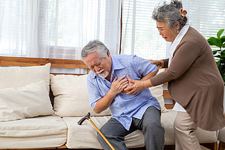 亚洲老人在客厅沙发上心痛 由妻子照顾 健康问题和生病概念