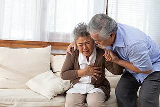 亚洲老年妇女在客厅沙发上心脏疼痛 由丈夫照顾 健康问题和身体<i>不</i><i>适</i>