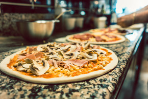 意大利餐厅厨房柜台上未烤披萨面团的特写 上面放着蘑菇 玉米 番茄酱和火腿