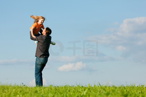 父亲和他的孩子 — 女儿 — 在草地上一起玩耍 他在夏末的午后将她扔到空中 家庭观念