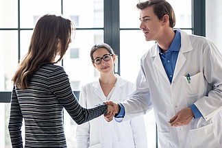 年轻<i>敬</i><i>业</i>的可靠医生和女病人在现代医疗中心办公室咨询前握手