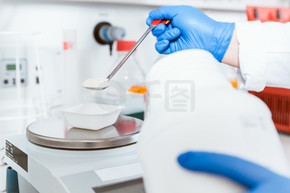 药剂师手戴蓝色手套在实验室秤上浇注白色粉末化学品的特写
