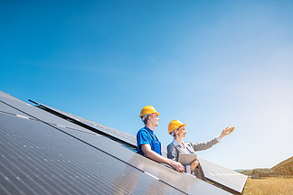 太阳能农场的<i>工</i>人和经理站在光伏板中望着太阳