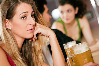 一群人在酒吧或餐厅喝啤酒 前面的女人很伤心 因为她的男朋友正在和另一个甩了她的女孩调<i>情</i>