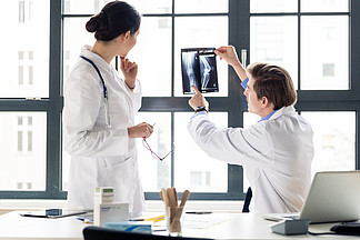 经验丰富的男性骨科医生帮助他的女同事解<i>释</i>办公室患者膝盖的 X 光片