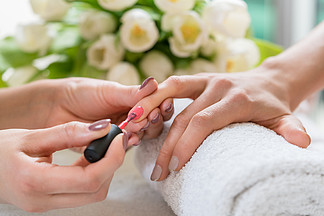 一位熟练的美甲师的手的特写 在时尚美容院的一位年轻女性的中等<i>长</i>度指甲上涂上优雅的红色指甲油