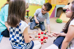 在一位年轻的幼儿园老师的指导下 可爱的学龄前男孩与同事合作建造由木制玩具积木制成的结构