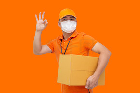 送货员拿着包裹箱 戴防护面罩 以防止 Covid-19 病毒 并在橙色背景下显示正常 在线购物发货和快速快递服务概念