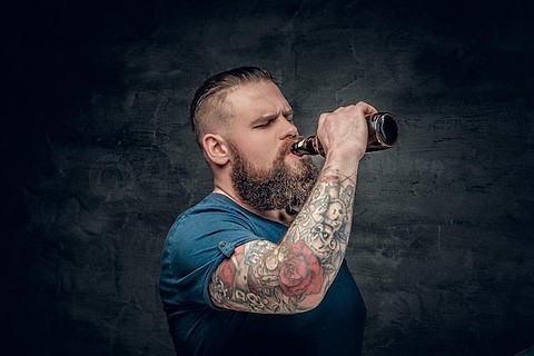 手臂上有纹身,留着胡子的胖男人喝着瓶子里的啤酒