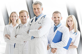 医生的成功的队看照相机并且微笑着，当站立与在医院时横渡的胳膊成功的医生团队