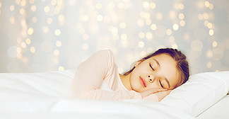 人，儿童，休息和舒适的概念— —假期在床上睡觉的女孩点<i>燃</i>背景在假期灯在床上睡觉的女孩