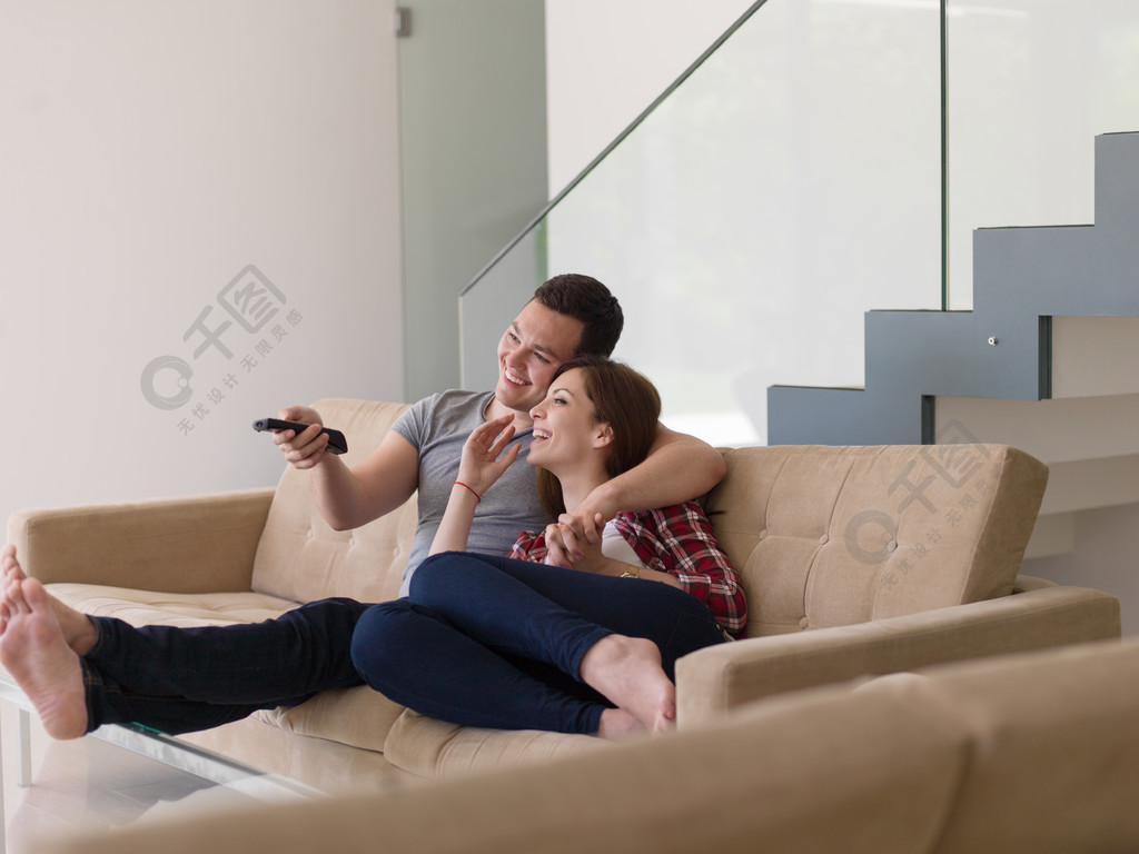 年轻的夫妇在沙发上一起看电视,在他们的豪华住宅